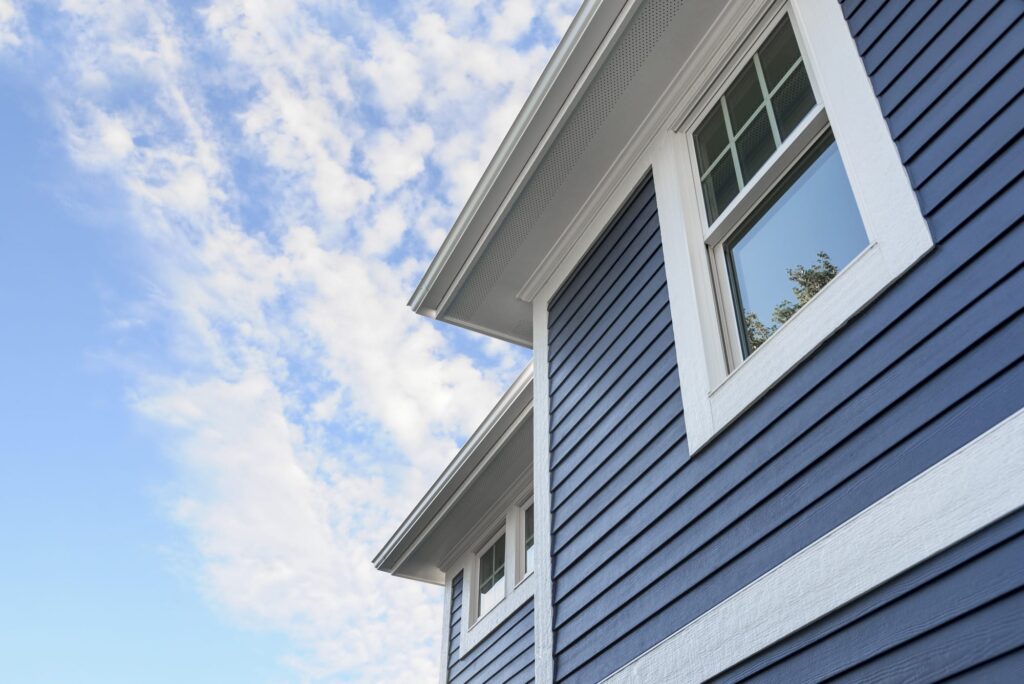 A close-up of a house with deep blue horizontal siding and crisp white trim under a bright blue sky, highlighting the clean, refreshed appearance after professional exterior cleaning in Findlay, OH.