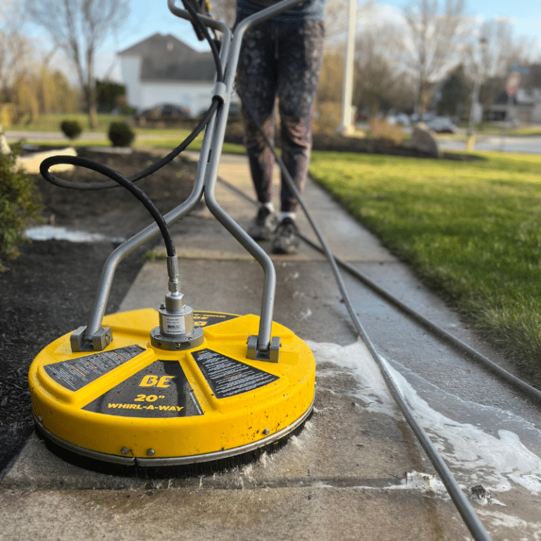A technician operates a surface cleaner on a driveway, with a branded service vehicle nearby, highlighting professional pressure washing services that enhance curb appeal and property value.