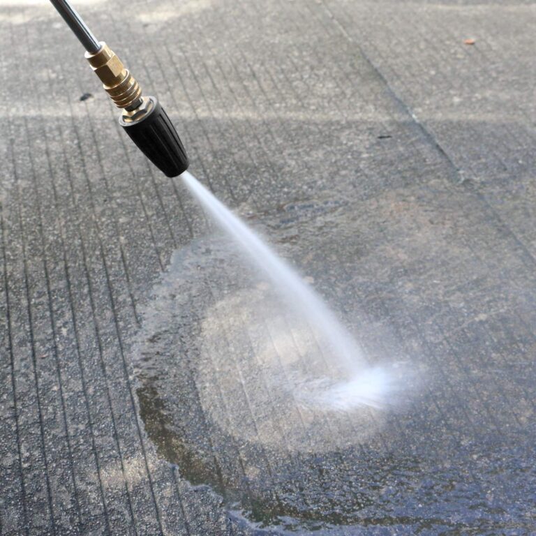 A close-up of a pressure washer nozzle cleaning a concrete surface, revealing a clean path and demonstrating the effectiveness of professional pressure washing techniques.
