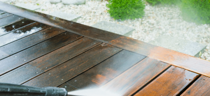 A close-up of a pressure washer cleaning a wooden deck, revealing rich wood tones and removing dirt and grime, highlighting effective outdoor surface restoration.