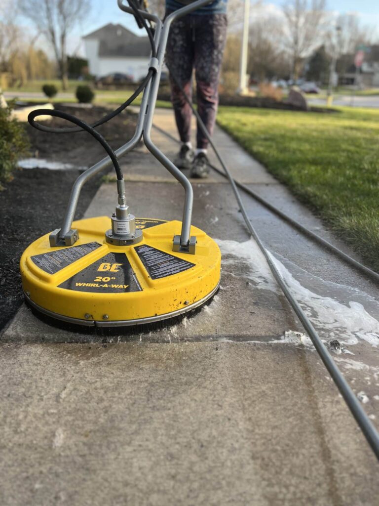 A technician uses a yellow 20-inch surface cleaner to wash a concrete sidewalk, creating a visible contrast between cleaned and uncleaned sections, demonstrating effective pressure washing services in Ottawa Hills, OH.