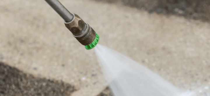 A close-up of a pressure washer nozzle cleaning a concrete surface, revealing a clean path and demonstrating the effectiveness of professional pressure washing techniques.