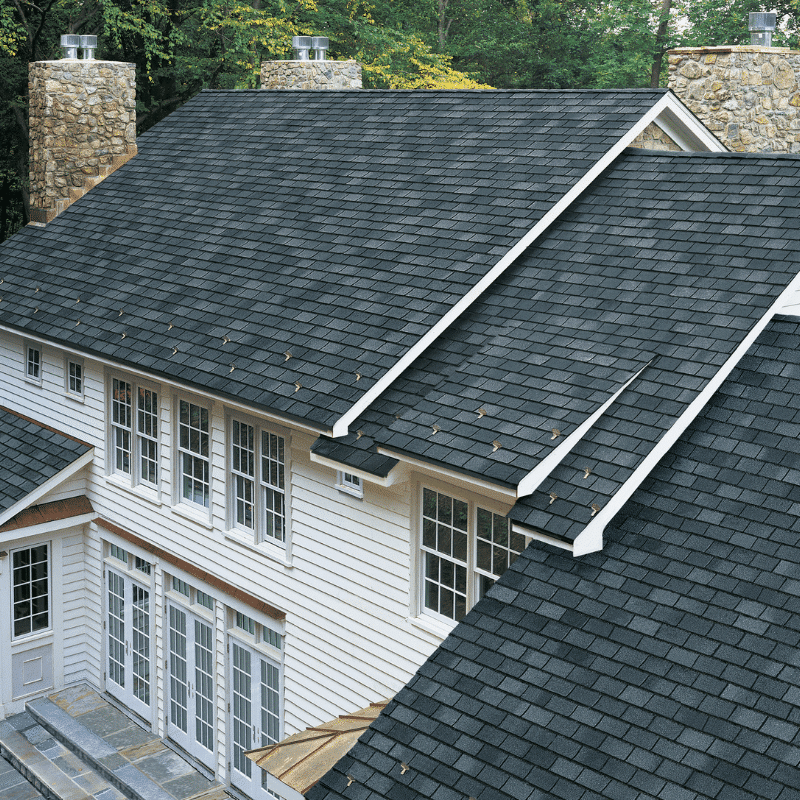 An aerial view of a clean, dark gray asphalt shingle roof on a white-sided home with stone chimneys, showcasing the results of expert roof cleaning in Bowling Green, OH.