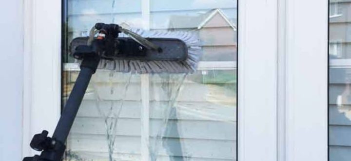 A water-fed pole with a brush attachment cleans a large window on a residential home, demonstrating a safe and effective method for exterior window washing without ladders or scaffolding.